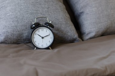 gri yastık ile kahverengi yatakta siyah çalar saat