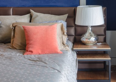 yatakta turuncu yastık ile ahşap masa üzerinde beyaz lamba 