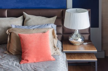 yatakta turuncu yastık ile ahşap masa üzerinde beyaz lamba 