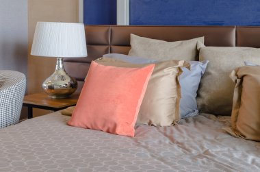 yatakta turuncu yastık ile ahşap masa üzerinde beyaz lamba 