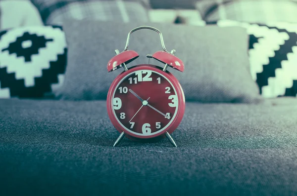 Foto retro estilo de reloj despertador rojo en la cama — Foto de Stock