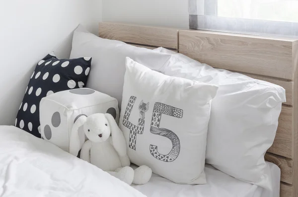 Black and white pillows with doll on wooden bed in kid's bedroom — Stock Photo, Image