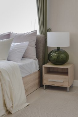 ahşap masa tarafında modern beyaz lamba ile yatakta beyaz yastıklar