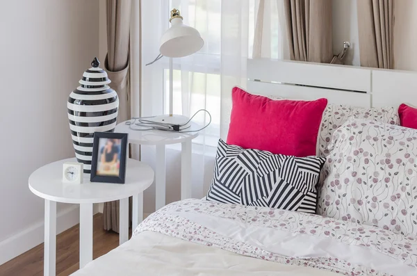 Κόκκινο μαξιλάρια σε λευκό ξύλινο κρεβάτι με σύγχρονη λάμπα — Φωτογραφία Αρχείου