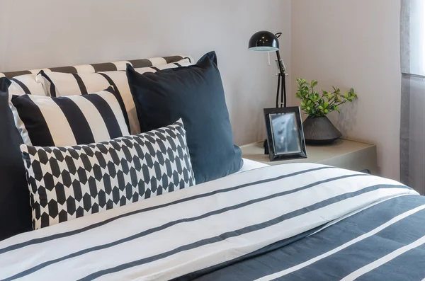 Black and white pillows and blanket on bed with black lamp on ta — Stock Photo, Image