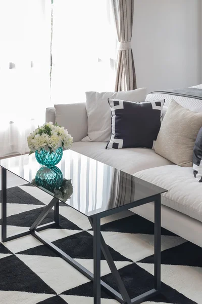 Florero de flores sobre mesa de cristal y sofá blanco con almohadas negras — Foto de Stock