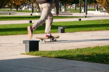 Bir çocuk güneşli bir günde parkta kaldırımda kaykaya biniyor.