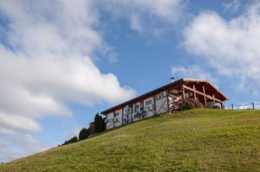 Küçük ahşap bir ev yeşil bir tepenin üzerinde duruyor.
