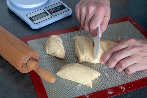 Rolling pin, a flexible plastic cutter, weighing machine. Hands cutting the dough.