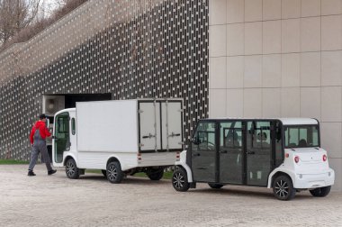 Krasnodar, Rusya - 22 Mart 2021: elektrikli minibüs duvara yakın duruyor ve şarj ediliyor. Sürücü binanın girişine doğru yürür..