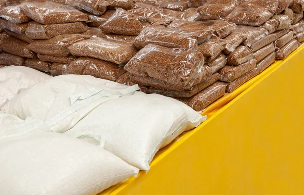 Many packages of buckwheat and sugar, flower on the shelf in shop. Package of buckwheat groats on supermarket shelf.