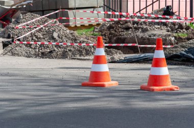 Koyu asfalt üzerinde parlak turuncu trafik konileri. Yoldaki delikte turuncu bir koni.