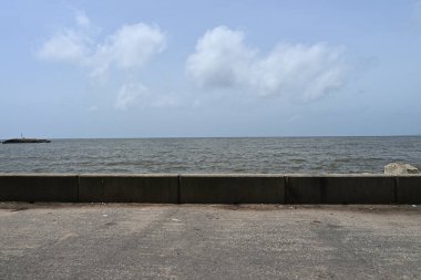 Arka planda deniz olan bir sahil yolunun kenarında küçük beton bir deniz manzarası.