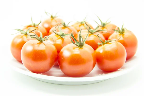 Onrijpe tomaten met groene leaf op witte plaat — Stockfoto