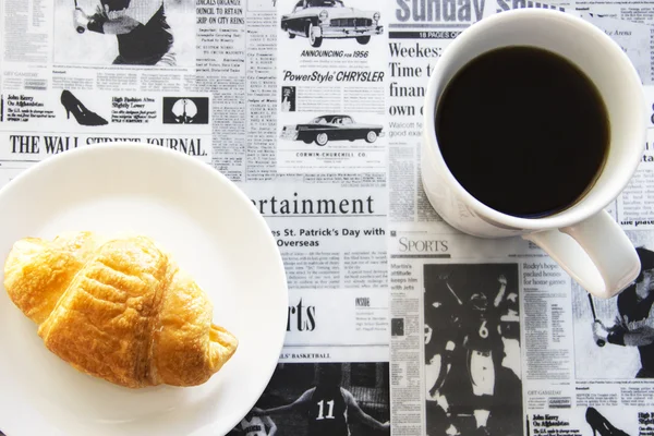 Croissant e caffè nero su sfondo giornale — Foto Stock