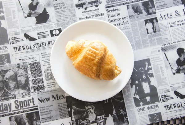 Fresh croissant on newspaper pattern — Stock Photo, Image