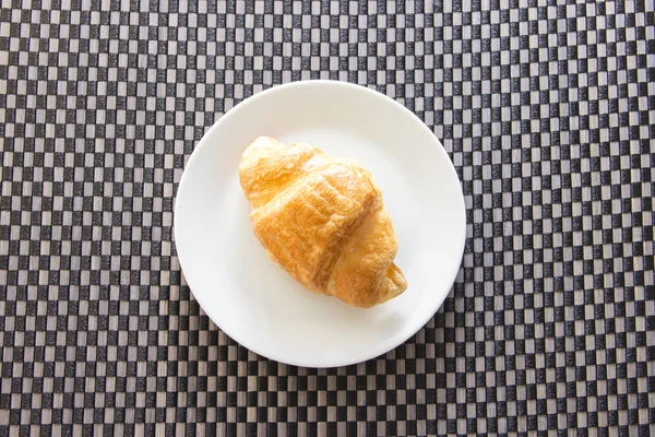 Croissant on plate contrast with mat pattern — Stock Photo, Image