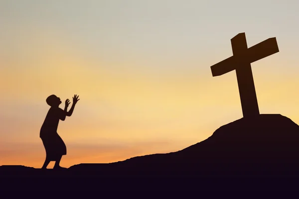 Conceito conceitual preto cruz ou religião símbolo homem silhueta em rochas sobre um céu por do sol com nuvens de luz solar fundo — Fotografia de Stock