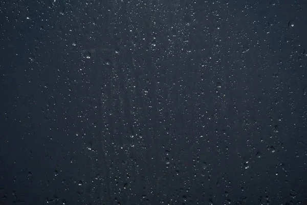 빗방울이 유리를 흘러내리고 저녁이 나가고 물방울은 전등에서 나오는 조명을 받는다 — 스톡 사진
