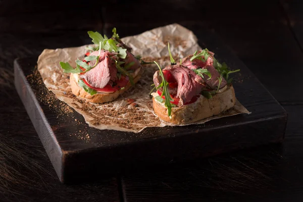 Bruschetta met rosbief en arugula op een houten plank — Stockfoto