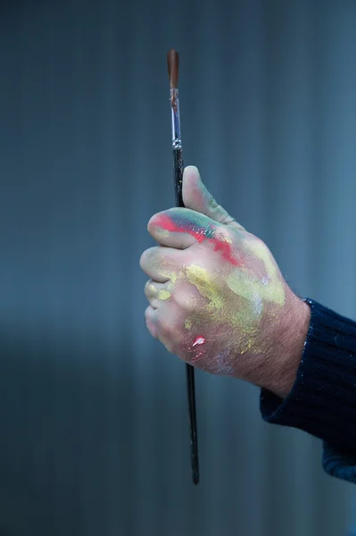 Bir fırça boya ile yakın çekim yakışıklı lekeli ellerini tutarak sanatçı
