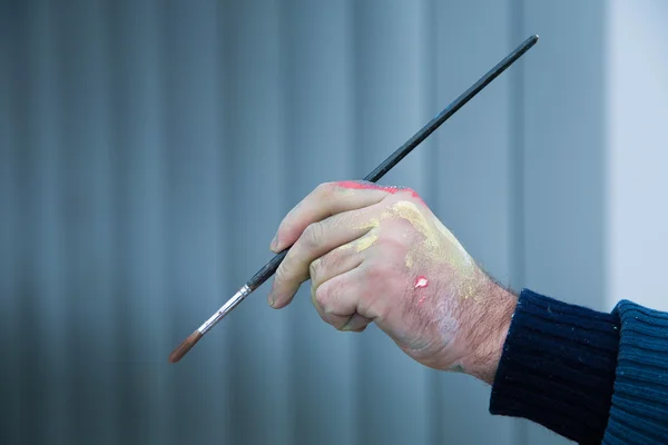 Bir fırça boya ile yakın çekim yakışıklı lekeli ellerini tutarak sanatçı