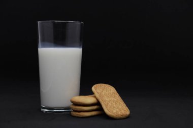 Temiz bir bardaktaki süt ve siyah arkaplanda kurabiyeler