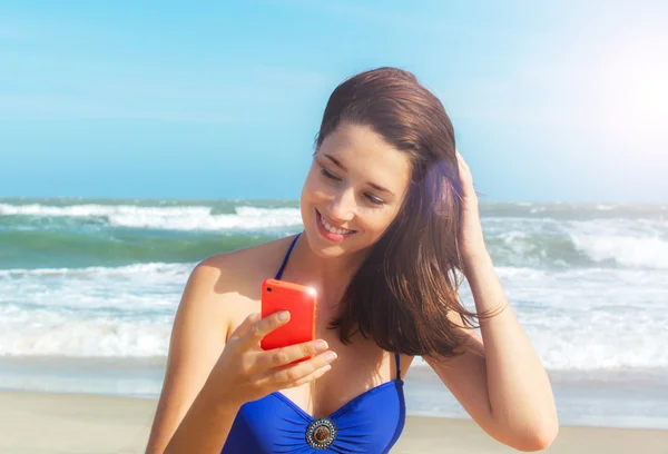 Mladá žena s mobilním telefonem na pláži — Stock fotografie