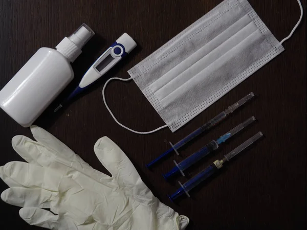Medical syringe, electronic thermometer, medical mask, disposable gloves and antiseptic on a black background