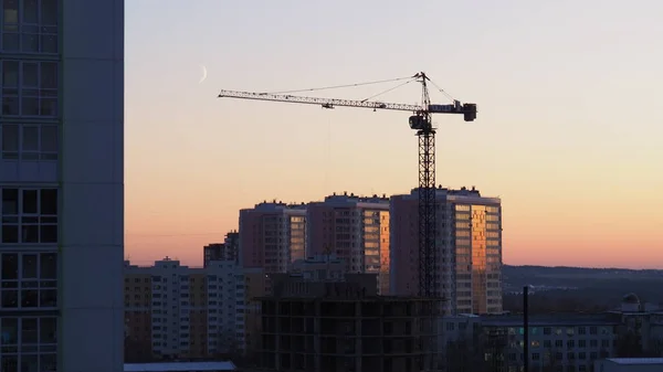 Building a house at sunset. Crane, silhouettes of workers.