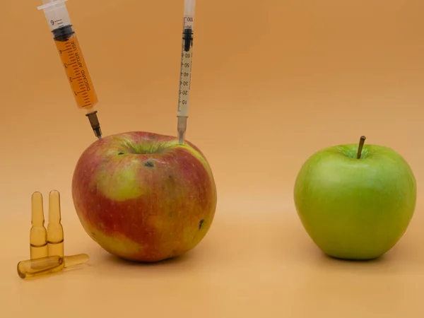 A genetically modified product. GMO red sick apple with a syringe and healthy green apple. Isolated against the gold fortune background.
