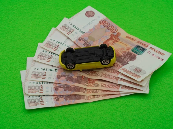 a yellow toy car is upside down on a stack of Russian money. Five thousand rubles, bills. The concept of a car accident, automobile repair, payment of road tax.