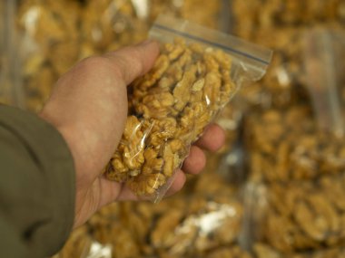 Elleri soyulmuş ceviz yarımlarını seçen bir adam marketin tezgahında, markette ya da pazarda tek tek paketlenmiş olarak bulunur. Koronavirüs sırasında ticaret kavramı, ürün güvenliği..