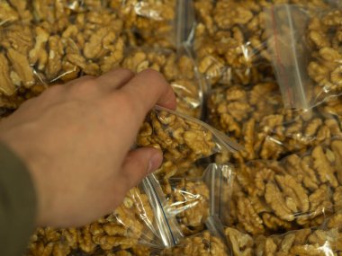 Elleri soyulmuş ceviz yarımlarını seçen bir adam marketin tezgahında, markette ya da pazarda tek tek paketlenmiş olarak bulunur. Koronavirüs sırasında ticaret kavramı, ürün güvenliği..