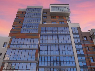 Binanın modern dış cephesi. İş yerinin camlı yüzü. Karmaşık geometrik ve renk, otelin gökdeleninin ahşap şekilleri. Günbatımının arka planındaki şehir evi pembe gökyüzü.