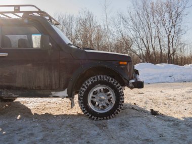 Bahar güneşinde toprak bir yola parketmiş bordo bir Rus SUV. Karda dört çeker bir arabanın 32 inçlik tekerlekleri. Sefer sepeti, raylar ve bariyerler arabada..