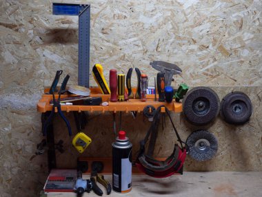 Garajdaki aletlerle birlikte rafta baskılı talaştan yapılmış kontrplak var. İngiliz anahtarı, tornavida, öğütücü tekerlek, mezura. Araba tamiri için gerekli donanıma sahip bir atölye konsepti.
