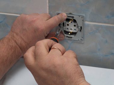 Ekonomik koca, elektrikçi, tamirat, banyoya priz kuruyor. Alyanslı adam eli, duvar seramik seramiklerinin arka planına yakın plan tornavidayla soketi çevirir..