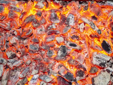 Kamp ateşinde yanan kömürün detaylı dokusu. Şöminede yanan közlerin arka planı. Yakacak odundan barbekü kömürü. Mangalda çevre dostu organik yakıtı ateşleyin..