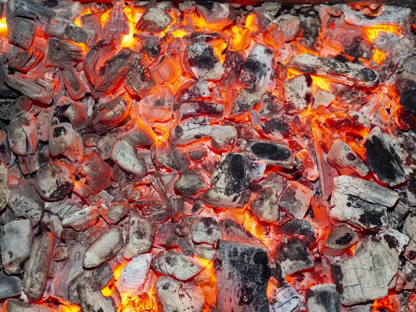 Detailed texture of burning charcoal in a campfire. Background of embers smouldering in the fireplace. Barbecue coals from firewood. Fire eco friendly organic fuel in grill top view.