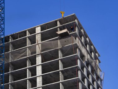 Modern bir ofis iş merkezi inşaatı, yüksek binalar. Bir kule vinci, sağlam mavi gökyüzüne karşı bir yerleşim gökdeleni inşa etmek için bir kablo ile çimento kovasını kaldırır. Geliştirme kavramı.
