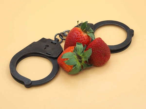 Polis metali kelepçeler ve sarı masa arkasında kırmızı olgun çilekler. 14 Şubat 'ta aşk ve kutlama kavramı. Kartpostal, sevgililer günü kartı.