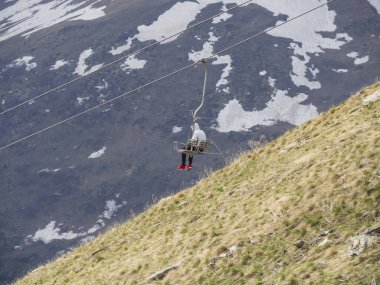Kırmızı spor ayakkabılı ve beyaz ceketli bir adam emniyet korkuluğunu indirmeden asansörden iner. Dombay Resort 'un Kafkasya dağlarının arka planında eski bir teleferik. Yalnızlık kavramı.