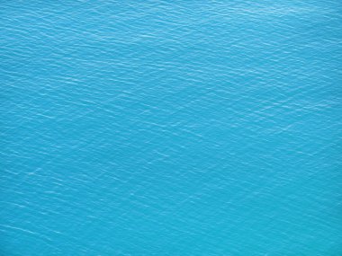 Sakin turkuaz deniz suyunun yüzey dokusu. Yukarıdan mavi, pürüzsüz okyanus manzaralı, havadan çekilmiş. Yeşil göl suyunun arka planı.
