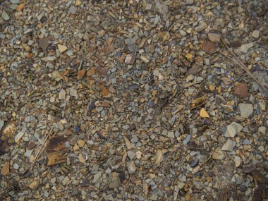 Doku kahverengi çakıllı toprak. Kayalık dağ eteklerinin arka planı. Çeşitli kahverengi ve kırmızı taşlar yakın plan..