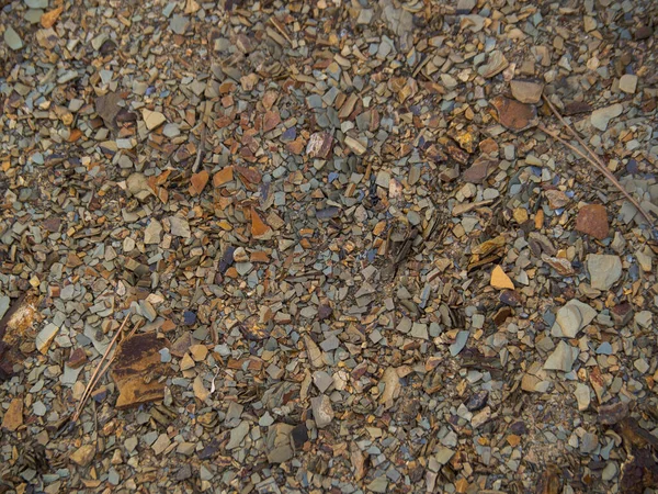 Doku kahverengi çakıllı toprak. Kayalık dağ eteklerinin arka planı. Çeşitli kahverengi ve kırmızı taşlar yakın plan..