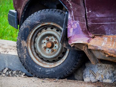 A car wrecked in an accident. A tire with a rusty disc on the curb after an emergency. Automobile wheel of a passenger machine close-up.