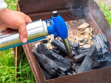 Adam elinde bir gaz ocağı tutuyor. Erkek, eski paslı bir barbeküde kömür yakar ve ateş yakar. Bahçenin arka bahçesinde hızlı bir öğle yemeği..