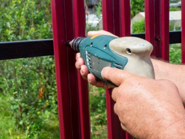 Bahçede bir çit inşa etmek. Matkap kullanan bir adam, çatıdaki çitlere vida takıyor. Özel bir bölge inşa etme ve geliştirme kavramı.