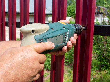 Bahçede bir çit inşa etmek. Matkap kullanan bir adam, çatıdaki çitlere vida takıyor. Özel bir bölge inşa etme ve geliştirme kavramı.